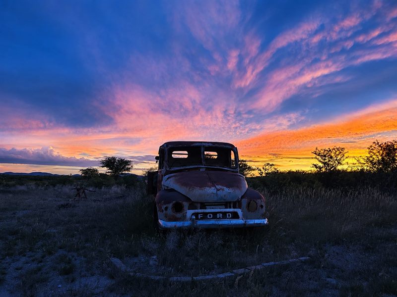 Sonnenuntergang über dem Damaraland mit einem alten Ford-Oldtimer im hohen Gras